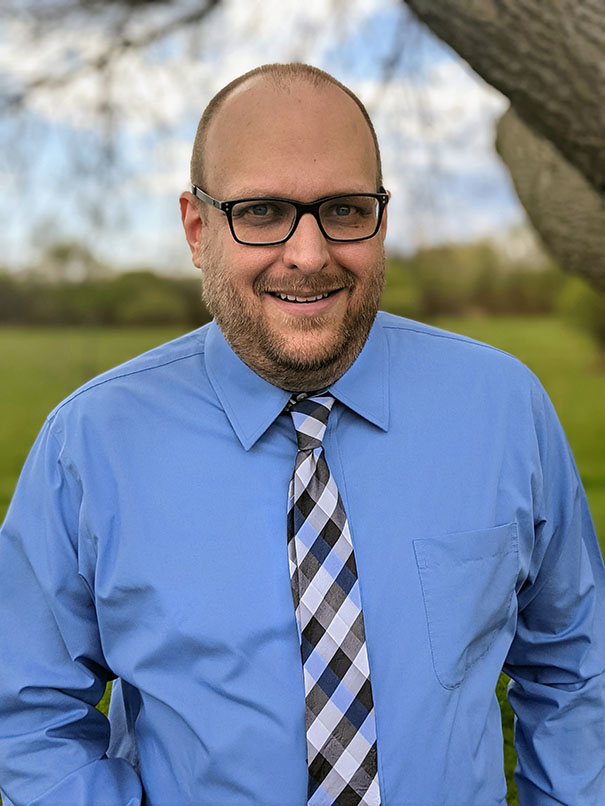 Photo of Jamie outdoors wearing a blue dress shirt and tie